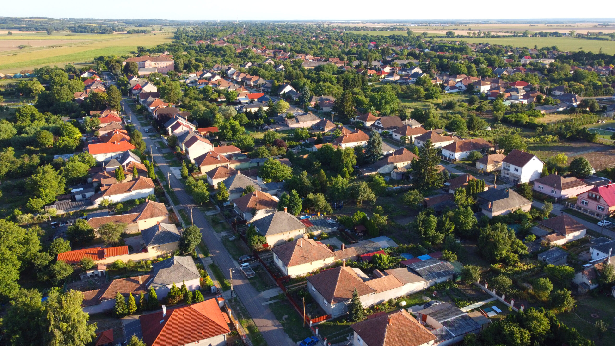 Aerial drone view of a peaceful rural village, traditional houses, red rooftops, and straight streets surrounded by lush greenery and open farmland. Eastern-European village. Balkan village. Hungary.